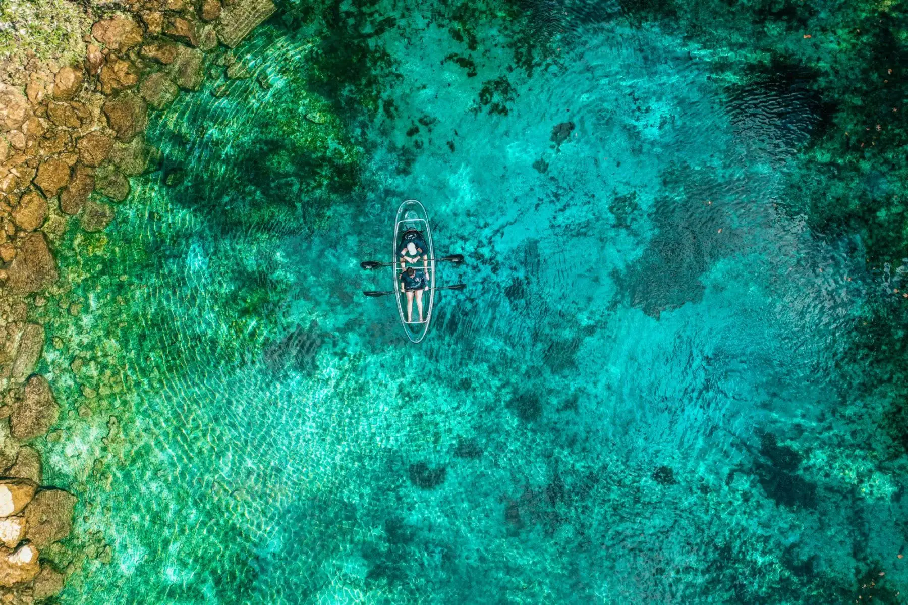 Aerial view of a single clear kayak on a bright blue spring