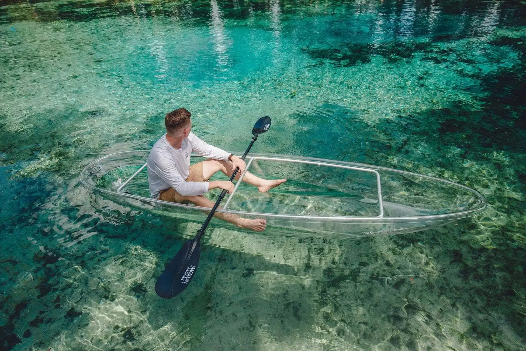 A paddler in a clear kayak drifting above green seagrass